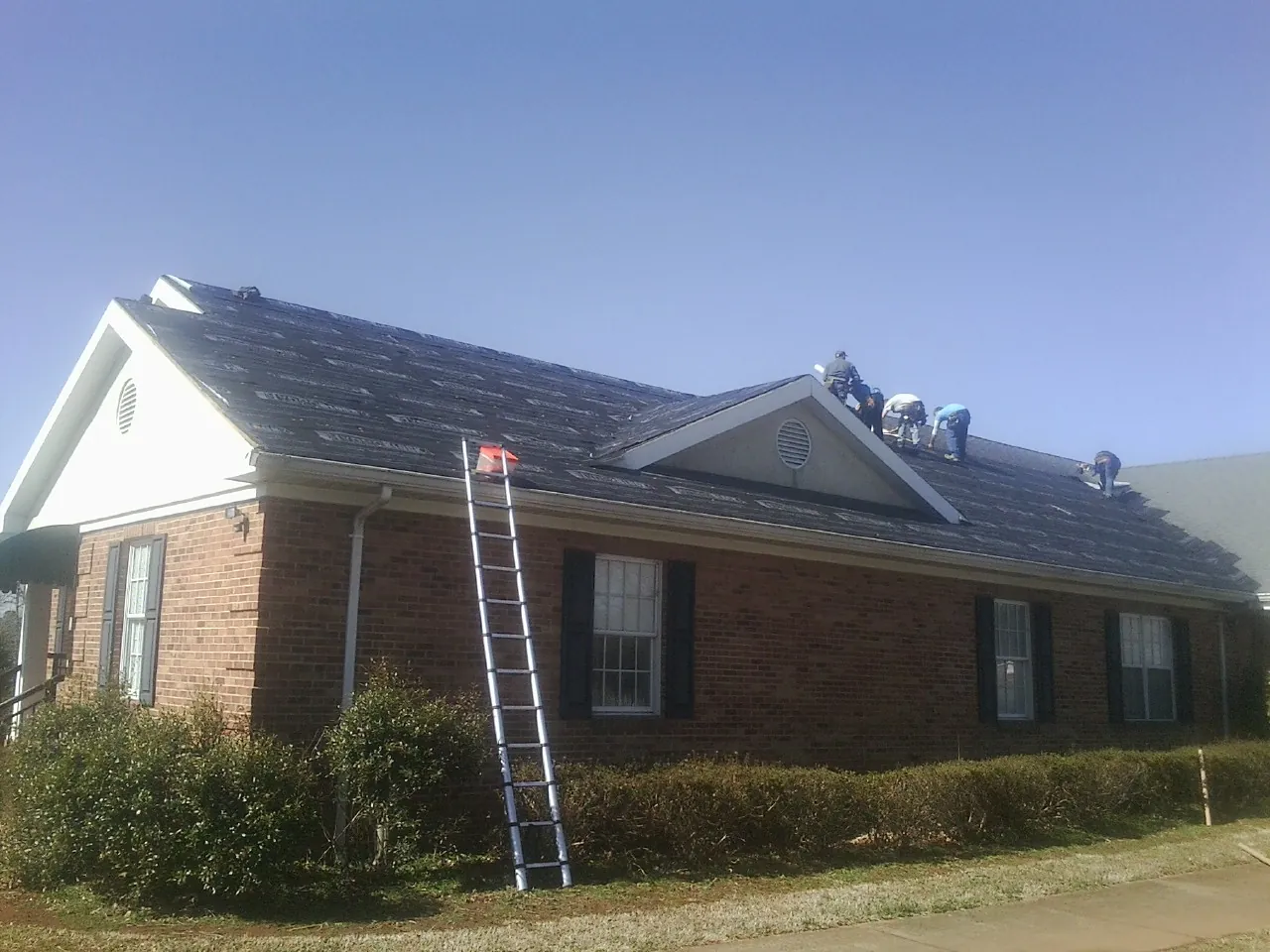Crew tearing shingles off a brick ranch roof with a ladder set — Emergency Roof Repair work by our crew in Whitmore