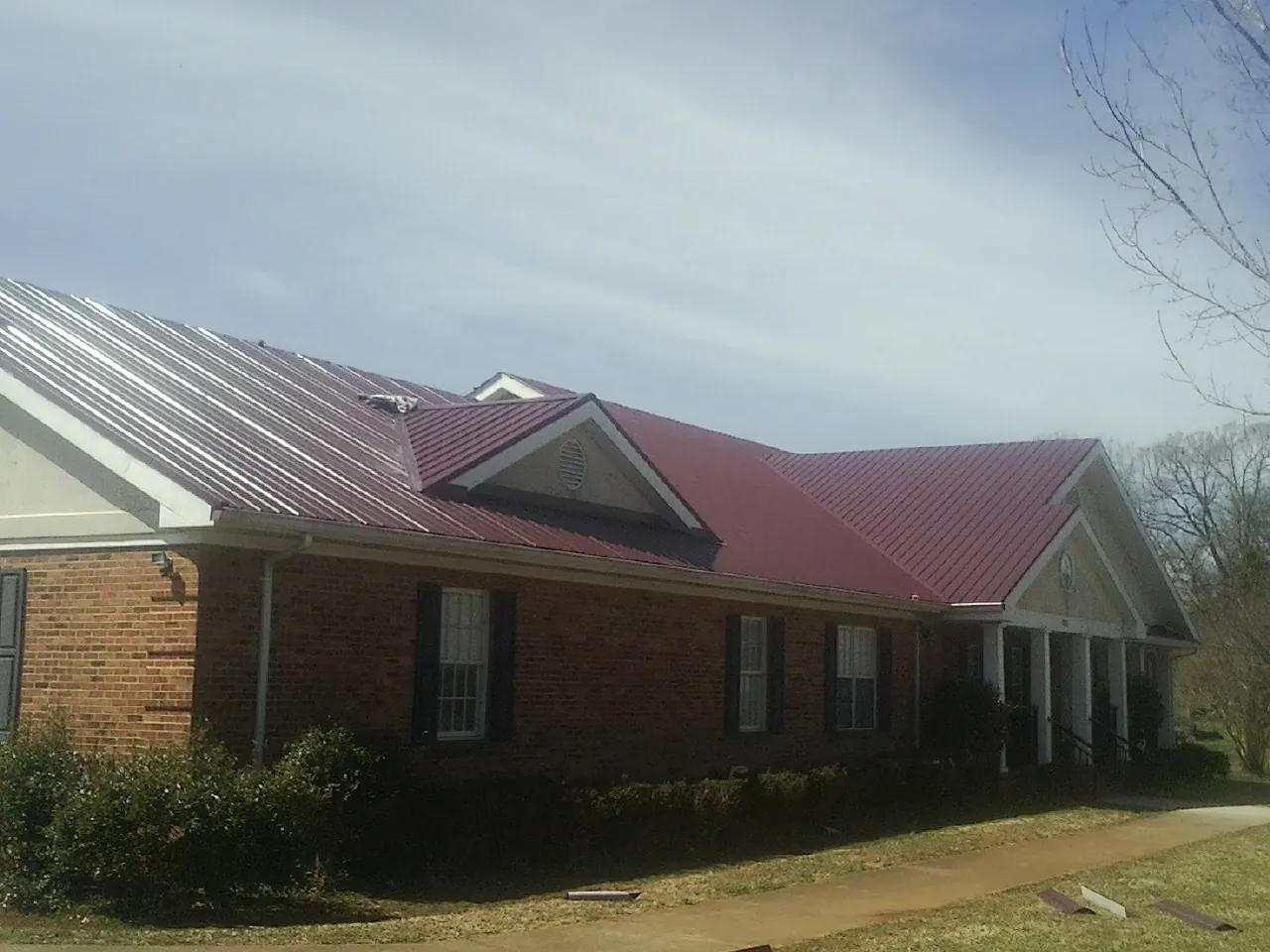 Red metal roof with gabled entries on a long brick building, from a Hail Damage Roof Repair job in Whitmore