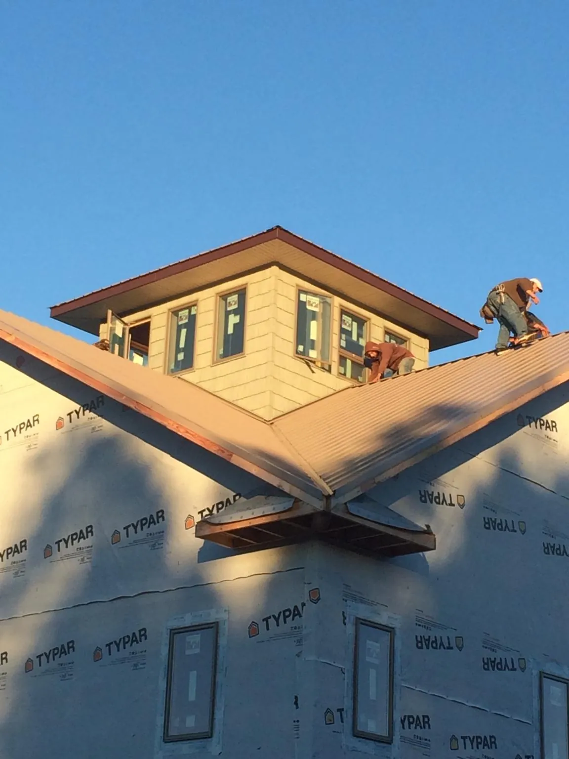 Roofers working around a rooftop cupola on a new metal roof at sunset — Roof Waterproofing in Whitmore by Roofing Brothers
